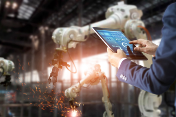 Man using a tablet in a factory to operate mechanical arms to do some welding work.