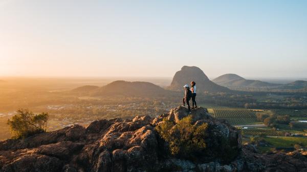 Two hikers stand on a hill-top looking into the distance. 