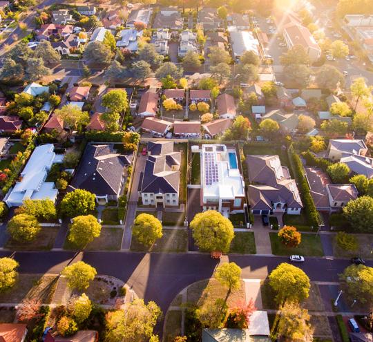 Birds eye view of a community, featuring roads, houses and trees.