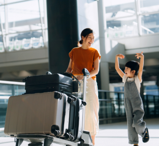 Mother and daughter walking through the airport terminal with their suitcases.