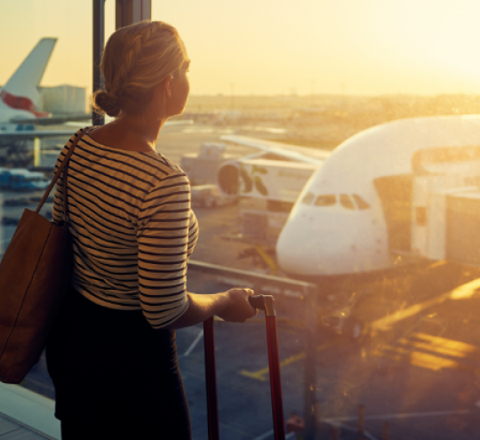 A woman looks out at a plane being loaded for a flight on the tarmac through an airport window.