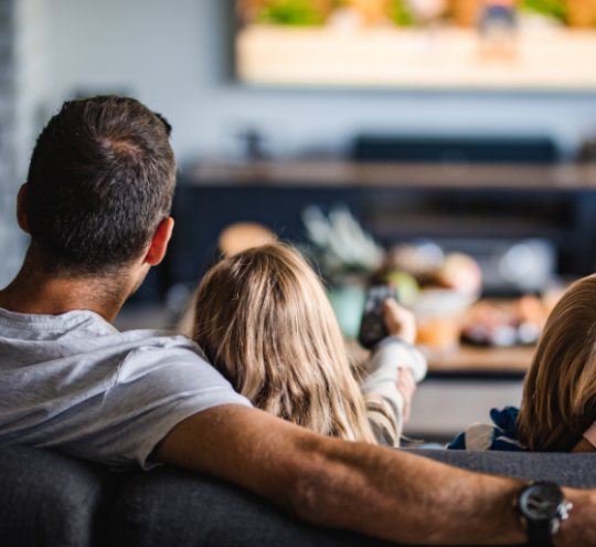 Family watching a screen on the wall in their home. Child using a remote.