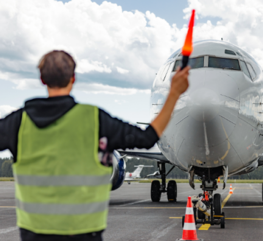 Aircraft marshal using two marshalling safety wands to signal the commercial airplane pilot. 