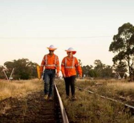 Workers in hi-vis clothing walk along regional train track.