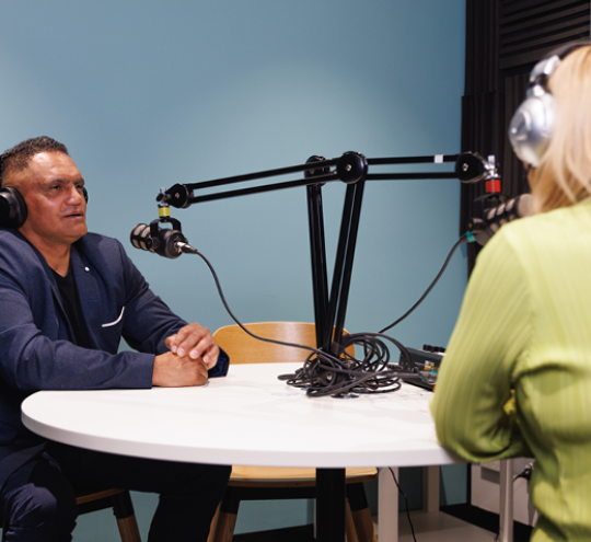 Man and woman wearing headphones and talking into microphones.