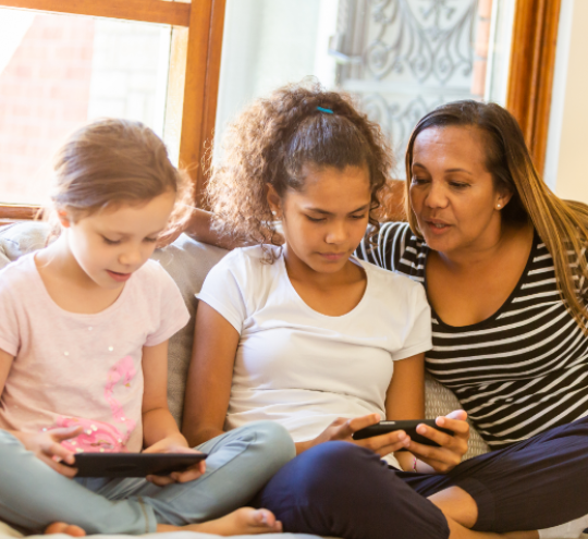 Mother sitting on a couch with two children who are using electronic devices.