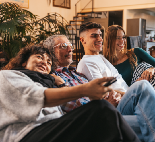 A multigenerational family sitting on a couch together watching television. 