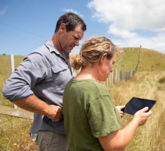 Two farmers in a field looking at information on a tablet device