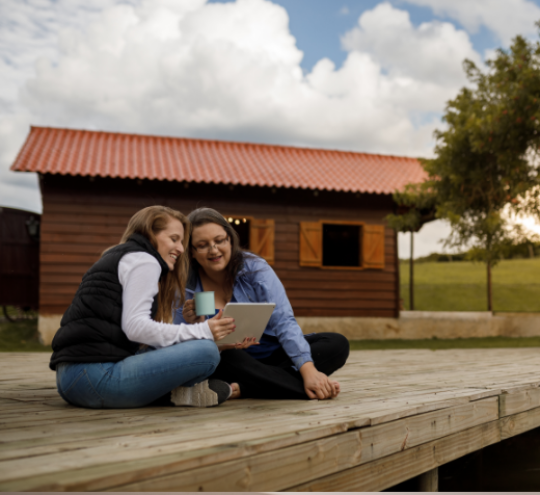 Two women on a deck, looking at a screen.