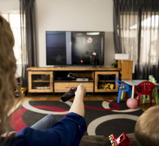 A mother and child sitting on a couch holding a remote up to the TV