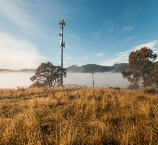 Mobile phone tower with blue cloudy sky in background and bushland in foreground