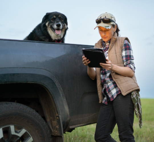 A female farmer leaning against her ute using her laptop