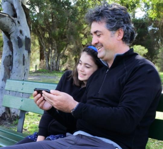 Father and daughter sitting on park bench looking at mobile phone