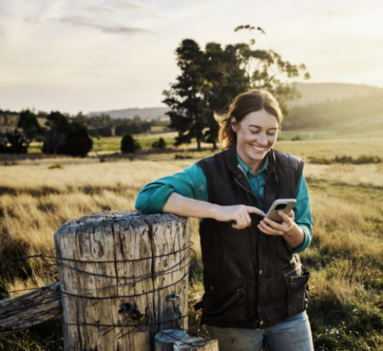 Women standing near a fence in the country, smiling whilst texting on her mobile phone 