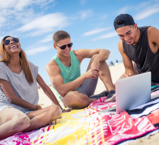 Three young friends looking at their laptop on the beach 