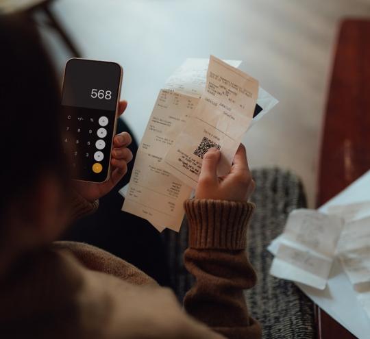 Person holding invoices and using calculator app on phone