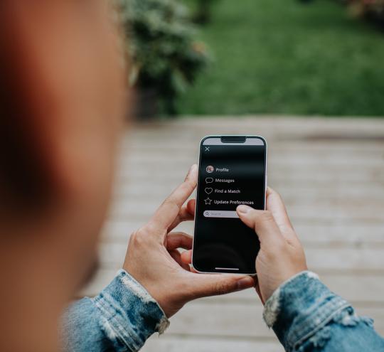 Man holds a smart phone, which shows a dating app.