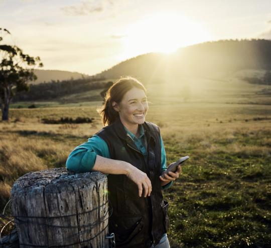 A woman holding a mobile phone on a farm.