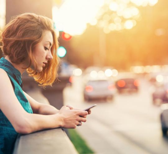 Woman using a mobile device in a city scene with cars driving past.