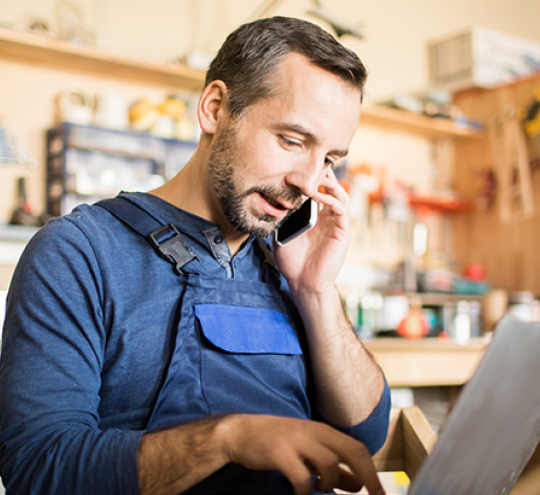 Male shopkeeper using a laptop and mobile device.