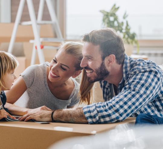 Two adults and a child sit around a table. The adults smiling and payning attention to the child.