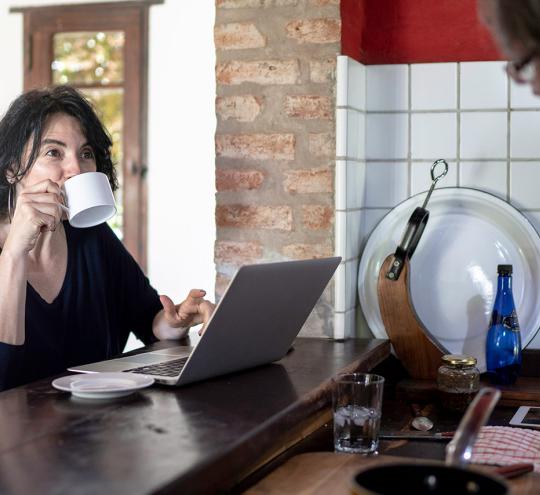 Woman drinking coffee at cafe bar with laptop in front of her. Man behind the cafe counter serving her.