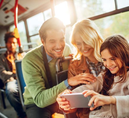 Young family on a bus looking at a mobile device.