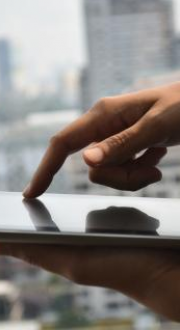 Person using a tablet in a high rise building looking out on to a city with tall buildings.