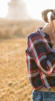 Woman farmer in a field talking on a mobile phone and looking at a mobile device in her left hand.