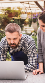 Man and woman looking at a laptop in a greenhouse environment.