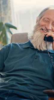 An older-aged man on a landline telephone is enjoying a casual conversation in his home.