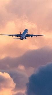 A passenger airplane silhouetted against sunset sky and clouds.