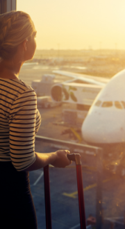 A woman looks out at a plane being loaded for a flight on the tarmac through an airport window.