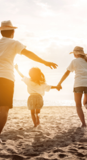 A family holiday hands and running on a beach with a kite and a car.