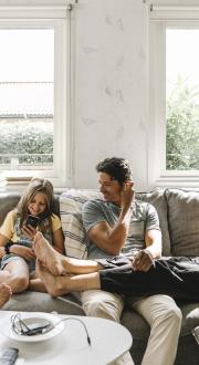 Happy family sitting on a couch in their living room, each using a device.