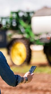 Farmer in a field looking at smartphone in front of a combine harvester.