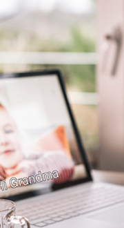 The screen of a lap top shows a young girl with the caption “Hi Grandma”. An elderly woman waves at the screen.