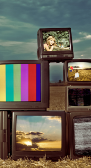 Several television sets showing various images sit in an open field 