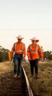 Workers in hi-vis clothing walk along regional train track.