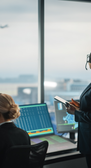 Image of two women behind control panels, one looking out at an airplane figure in the sky, one is looking at a desktop.