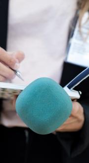 Journalist holding a microphone, notepad and pen.