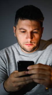 Man sitting in a dark room looking at his smartphone.