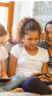 Mother sitting on a couch with two children who are using electronic devices.