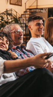 A multigenerational family sitting on a couch together watching television. 