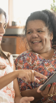 First Nations mother and daughter sitting on sofa at home pointing at a tablet