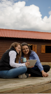 Two women on a deck, looking at a screen.