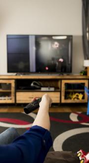 A mother and child sitting on a couch holding a remote up to the TV