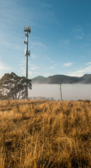 Mobile phone tower with blue cloudy sky in background and bushland in foreground