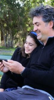 Father and daughter sitting on park bench looking at mobile phone