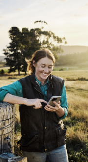 Women standing near a fence in the country, smiling whilst texting on her mobile phone 